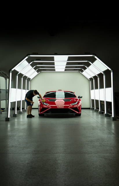 Red sports car in a lit garage tunnel, with a person leaning near the front left side.
