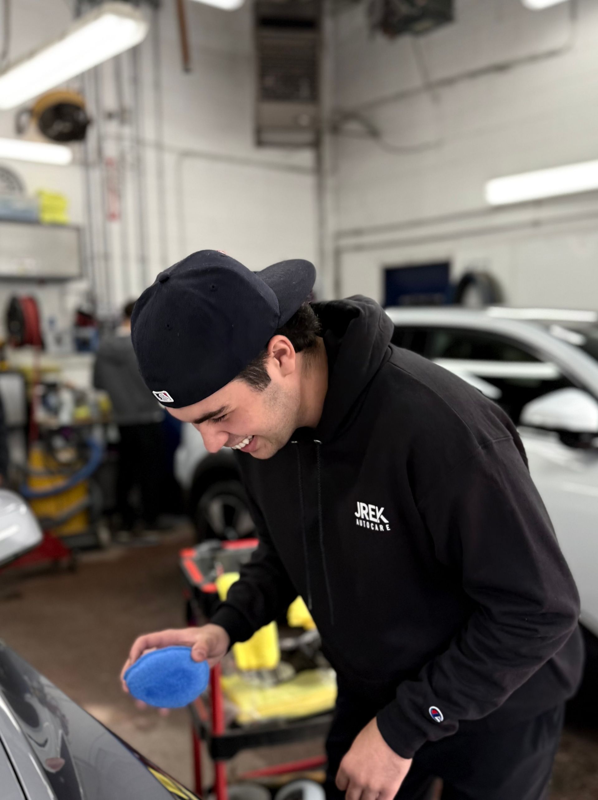 Man in a black hoodie and cap polishing a car in an auto shop