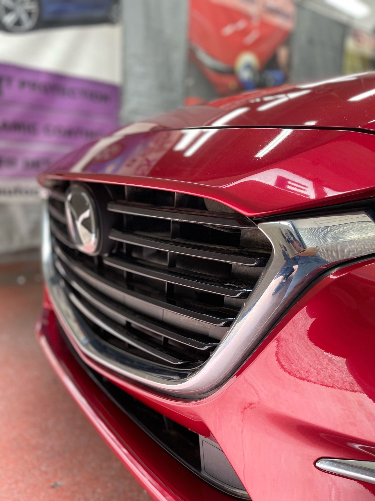 A close-up of the front grille and emblem of a shiny red Mazda vehicle.