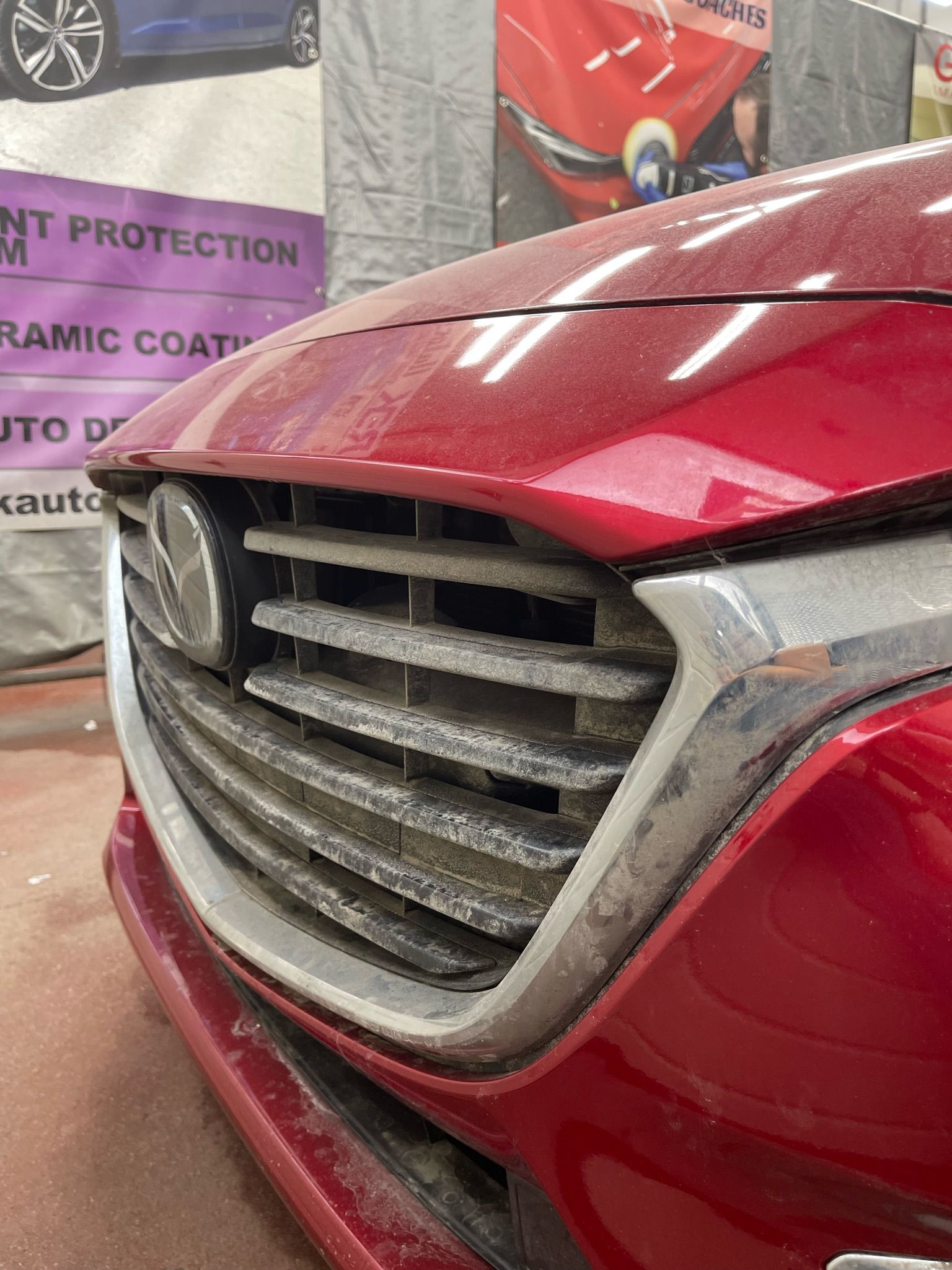 A close-up view of the front grill and red hood of a Mazda vehicle, showing water spots and light grime.