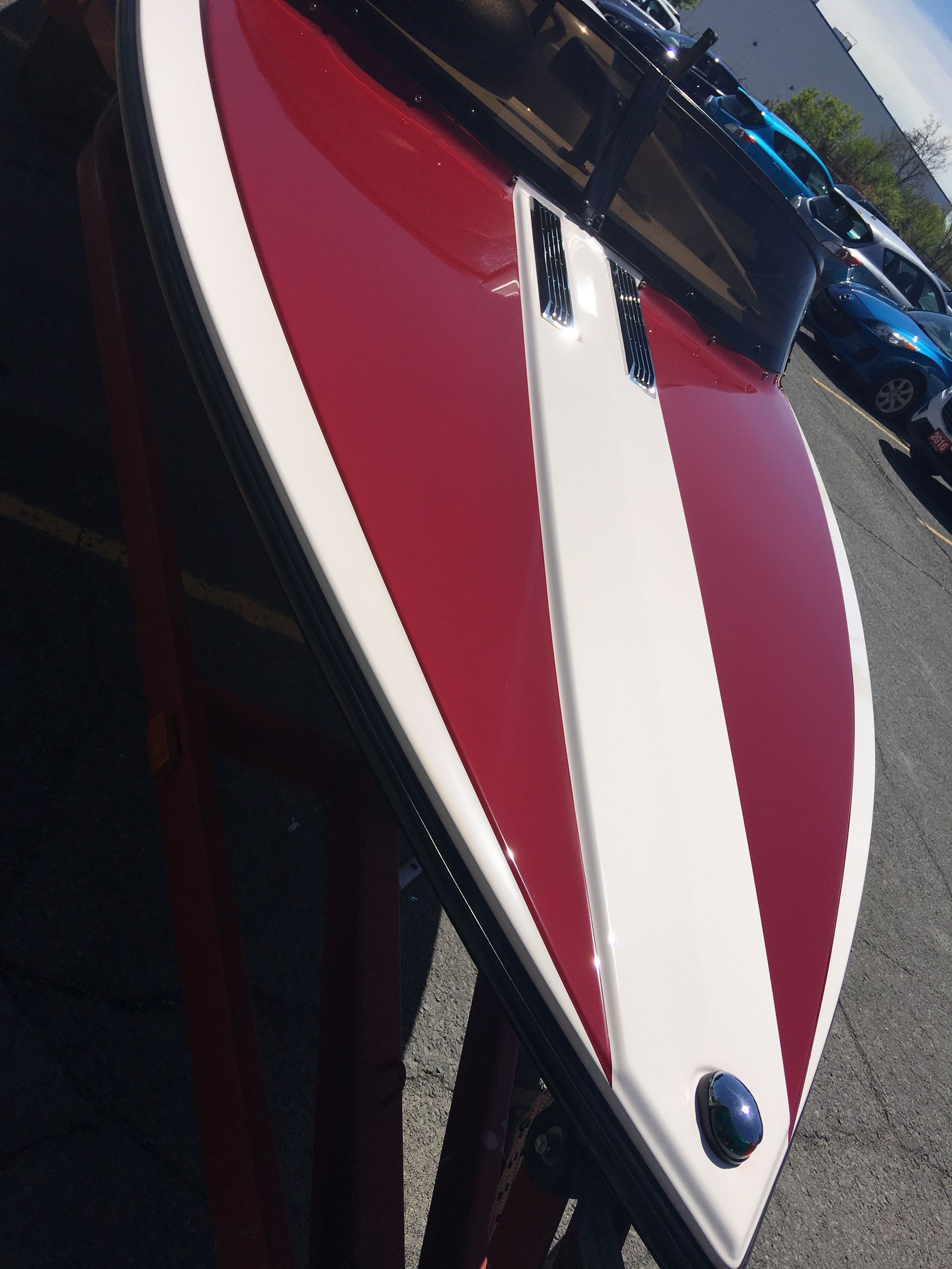 Red and white speedboat hull with a white stripe down the center, parked outdoors.
