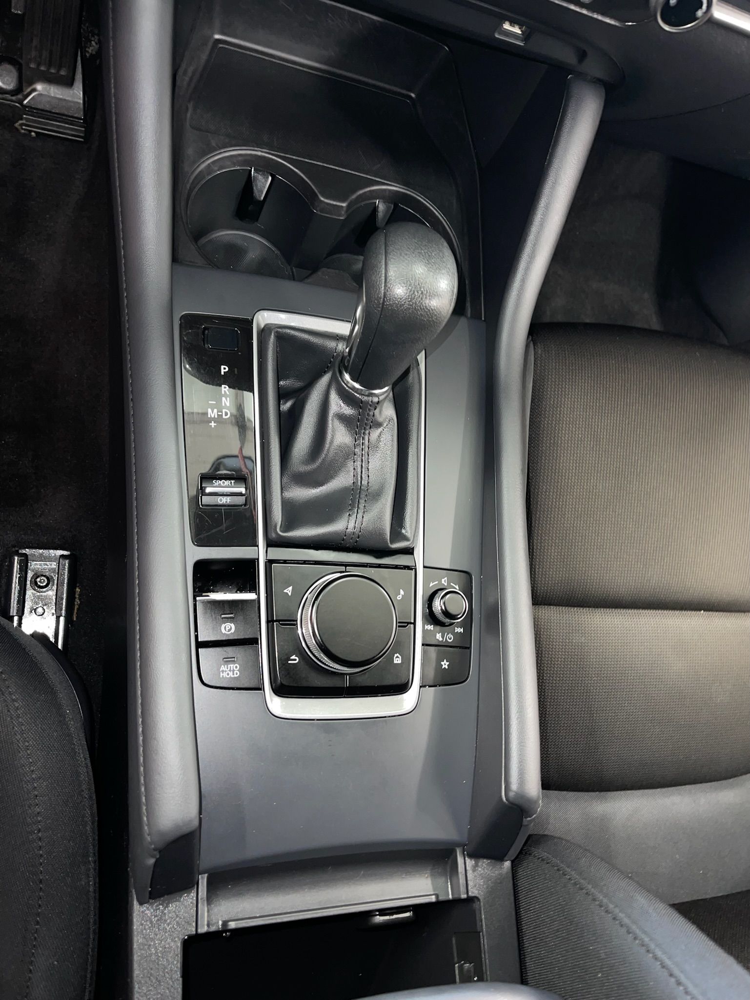 Center console of a car; black gear shift, cup holder, and control panel. Gray and black interior, visible dirt.