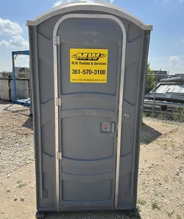A portable toilet with a yellow sign on it is sitting in a dirt field.