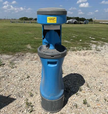 A blue trash can is sitting in the middle of a grassy field.