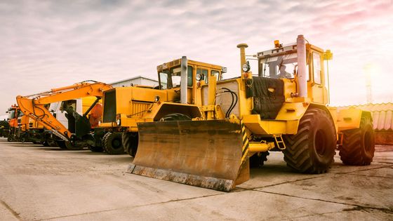 A row of yellow construction vehicles are parked in a parking lot.
