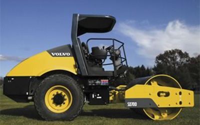 A yellow and black volvo road roller is parked in a grassy field