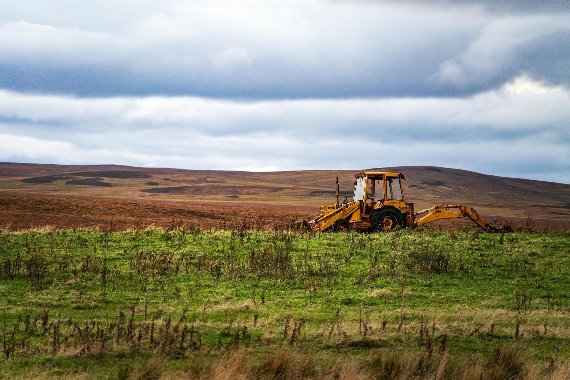 A yellow tractor is sitting in the middle of a grassy field.
