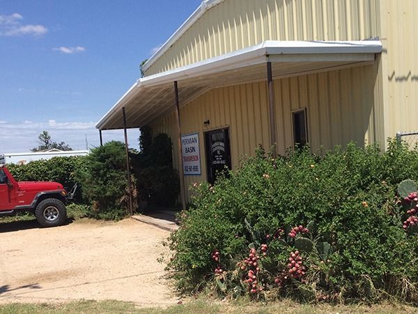 Yellow metal building entrance with a red truck parked beside bushes and pink flowers