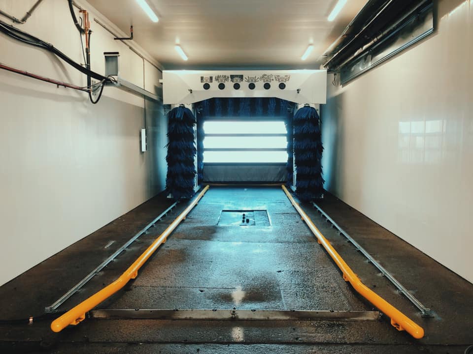 Empty car wash tunnel with yellow guide rails and bright lights at the exit