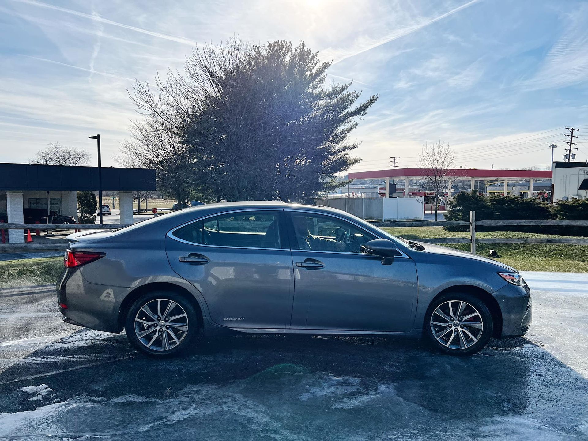 Gray sedan parked in a snowy lot with a bright sun and building in the background