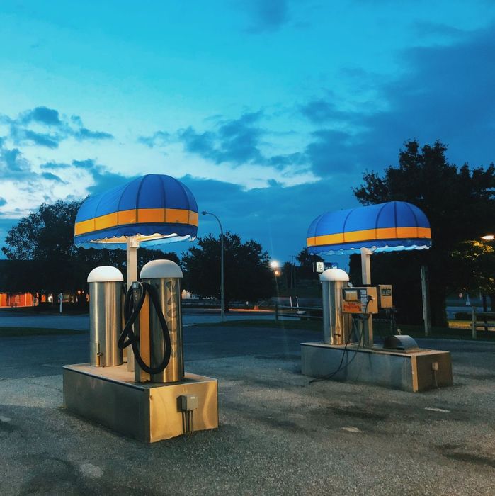 Two vintage gas pumps with blue-and-yellow canopies at dusk in a parking lot