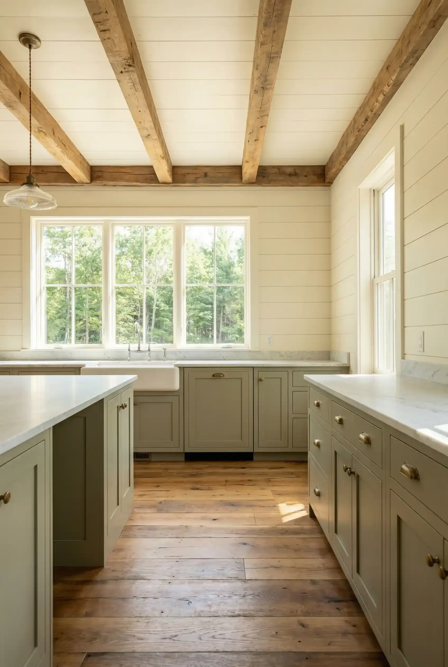 Bright farmhouse kitchen with white cabinets, wood beams, and large windows over a wooden floor