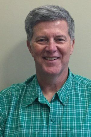 A man in a green plaid shirt is smiling for the camera. A man in a green plaid shirt is smiling for the camera.