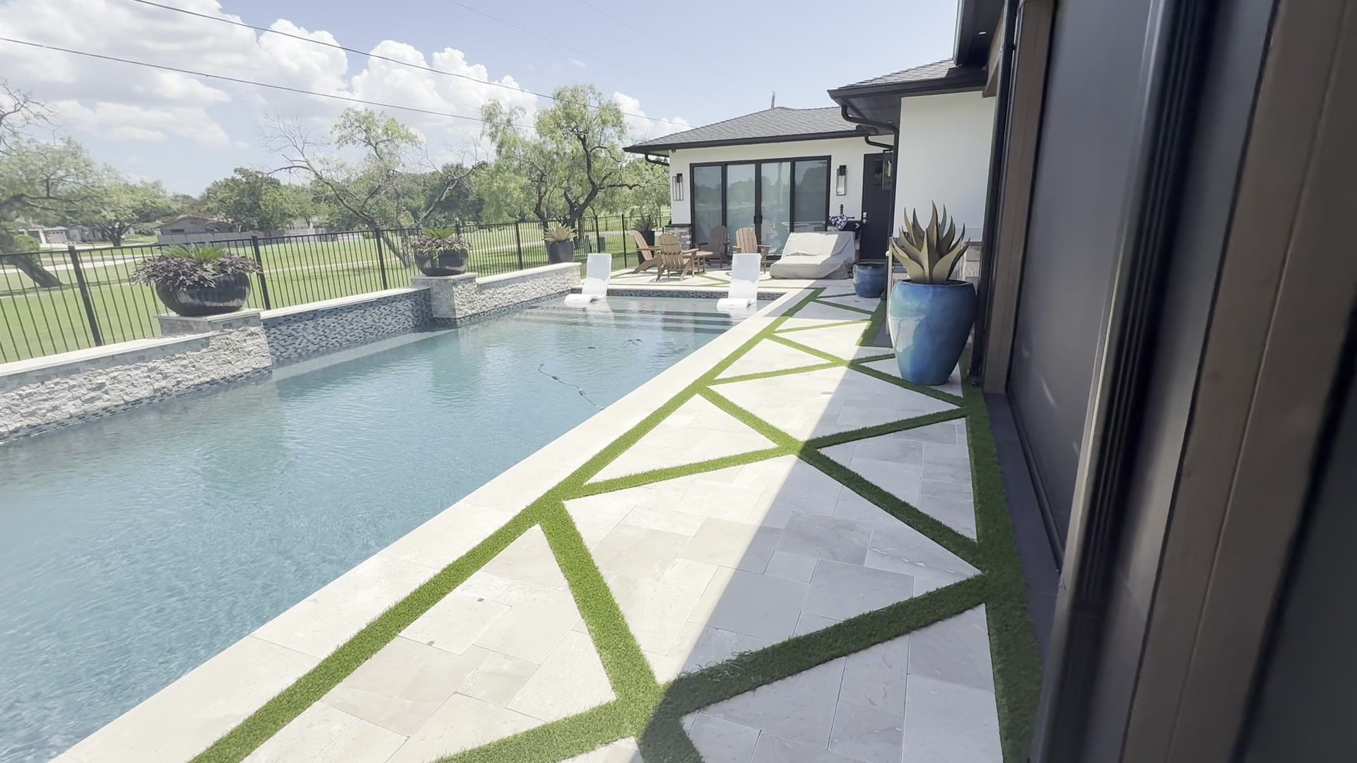Modern backyard pool with geometric stone patio and a house beside it