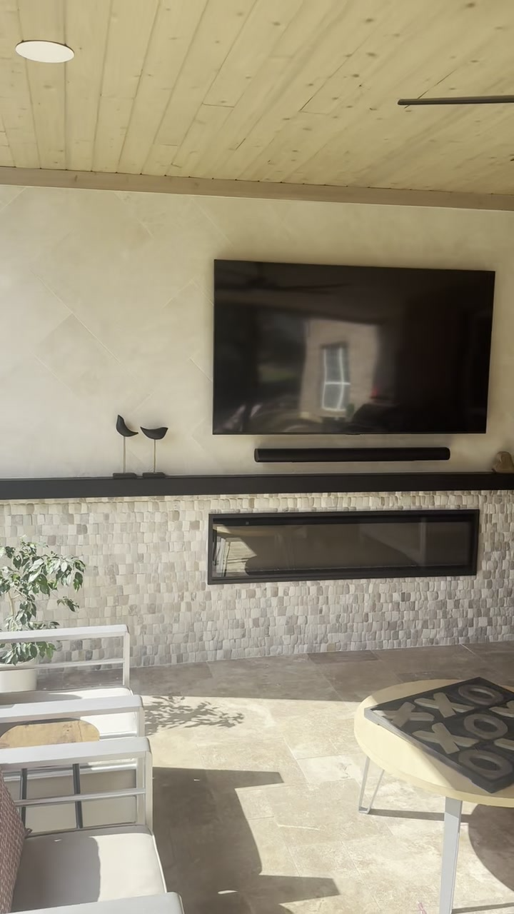Covered patio with wall-mounted TV, stone fireplace, and outdoor chairs and table