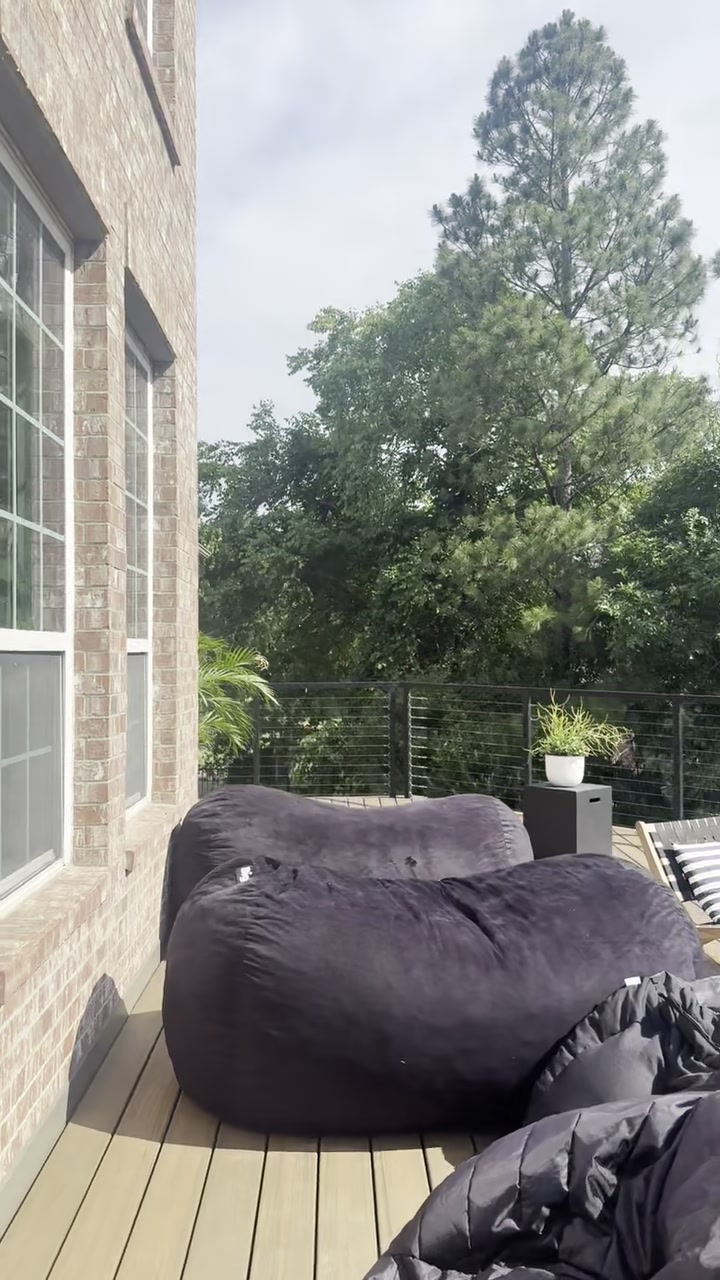 Patio deck with a black bean bag chair, potted plant, and trees beyond a railing