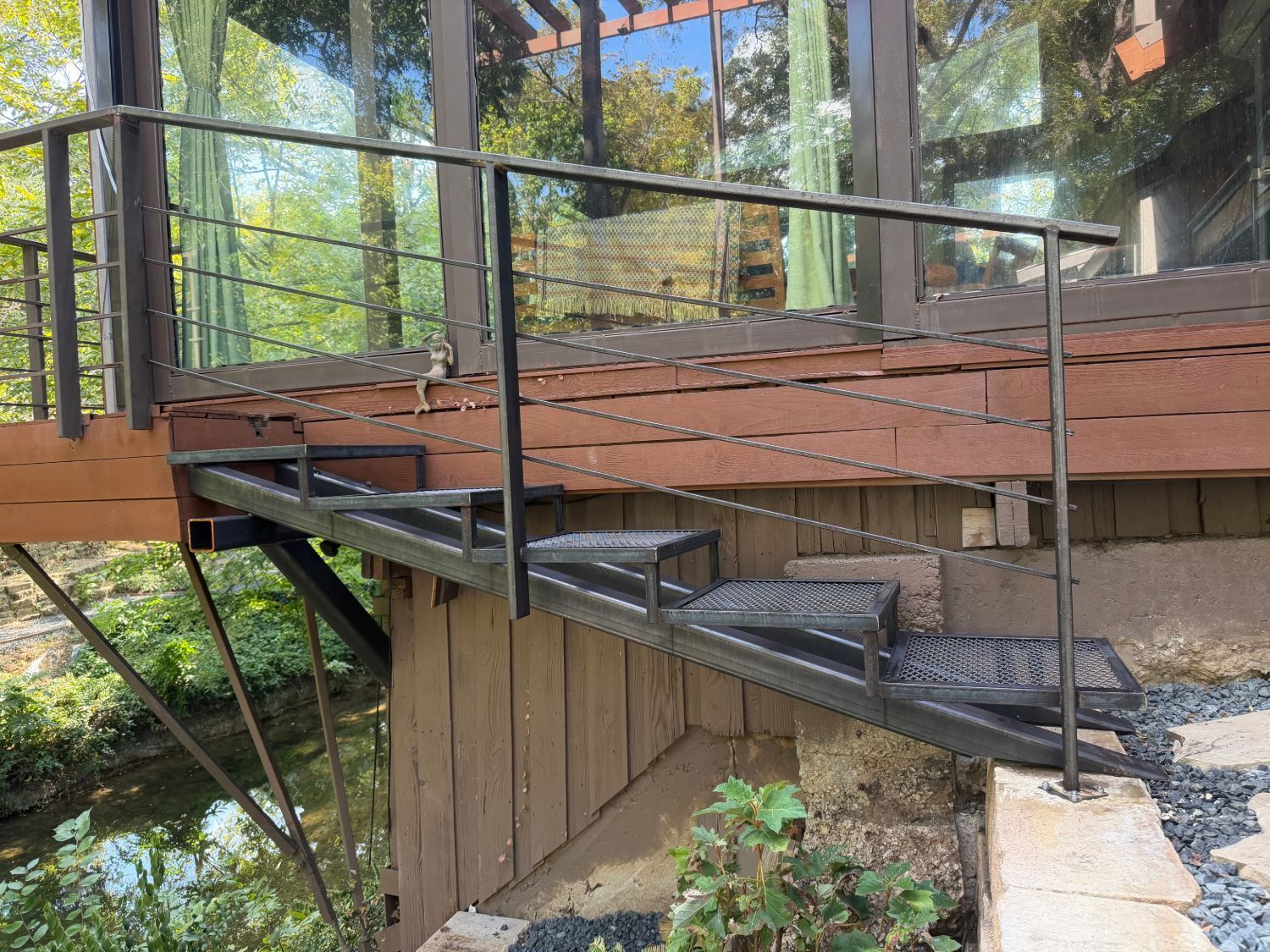 Wooden ramp with black railing leading to a raised deck in a wooded outdoor setting