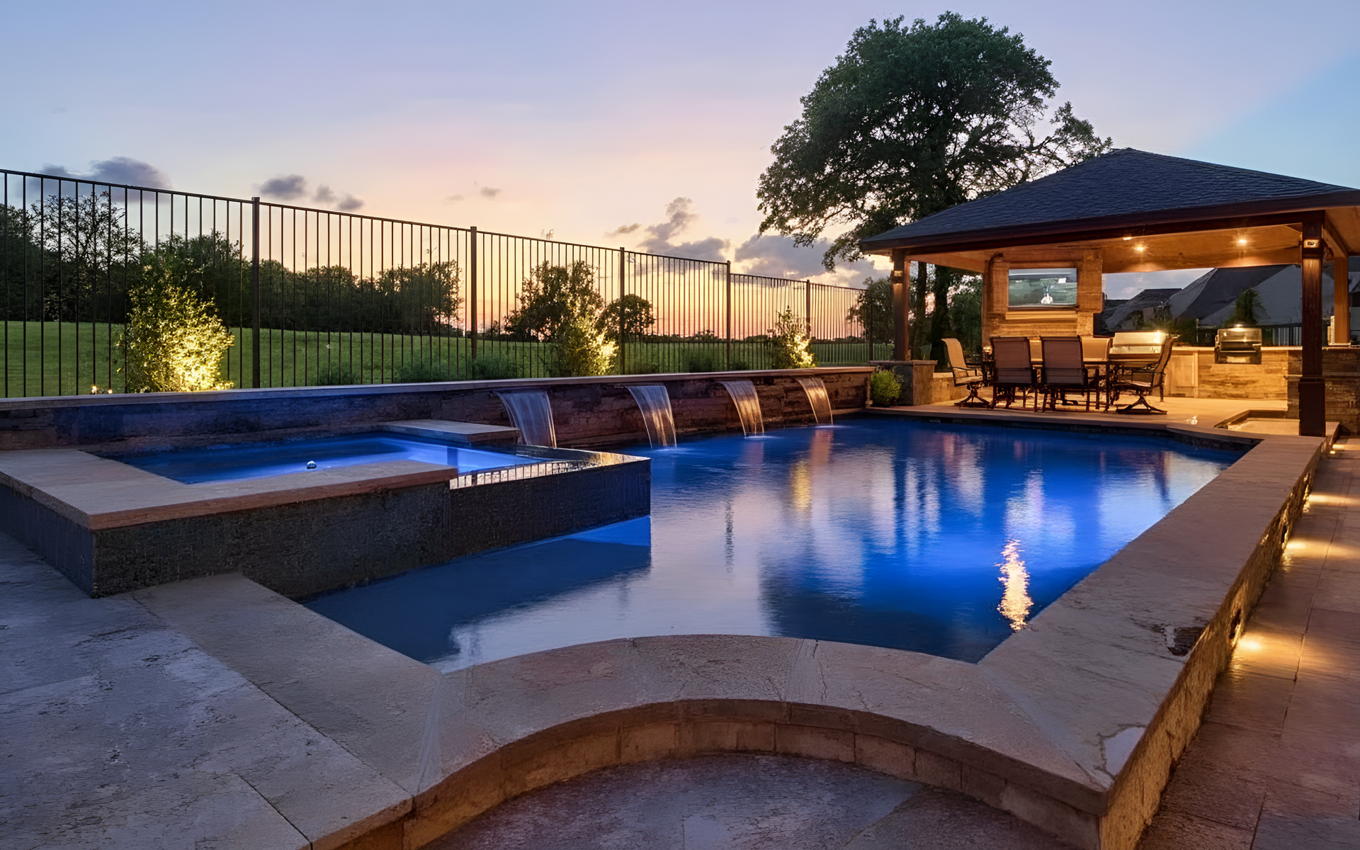 Backyard pool at sunset with a lit gazebo and lounge seating, reflecting blue water and warm lights