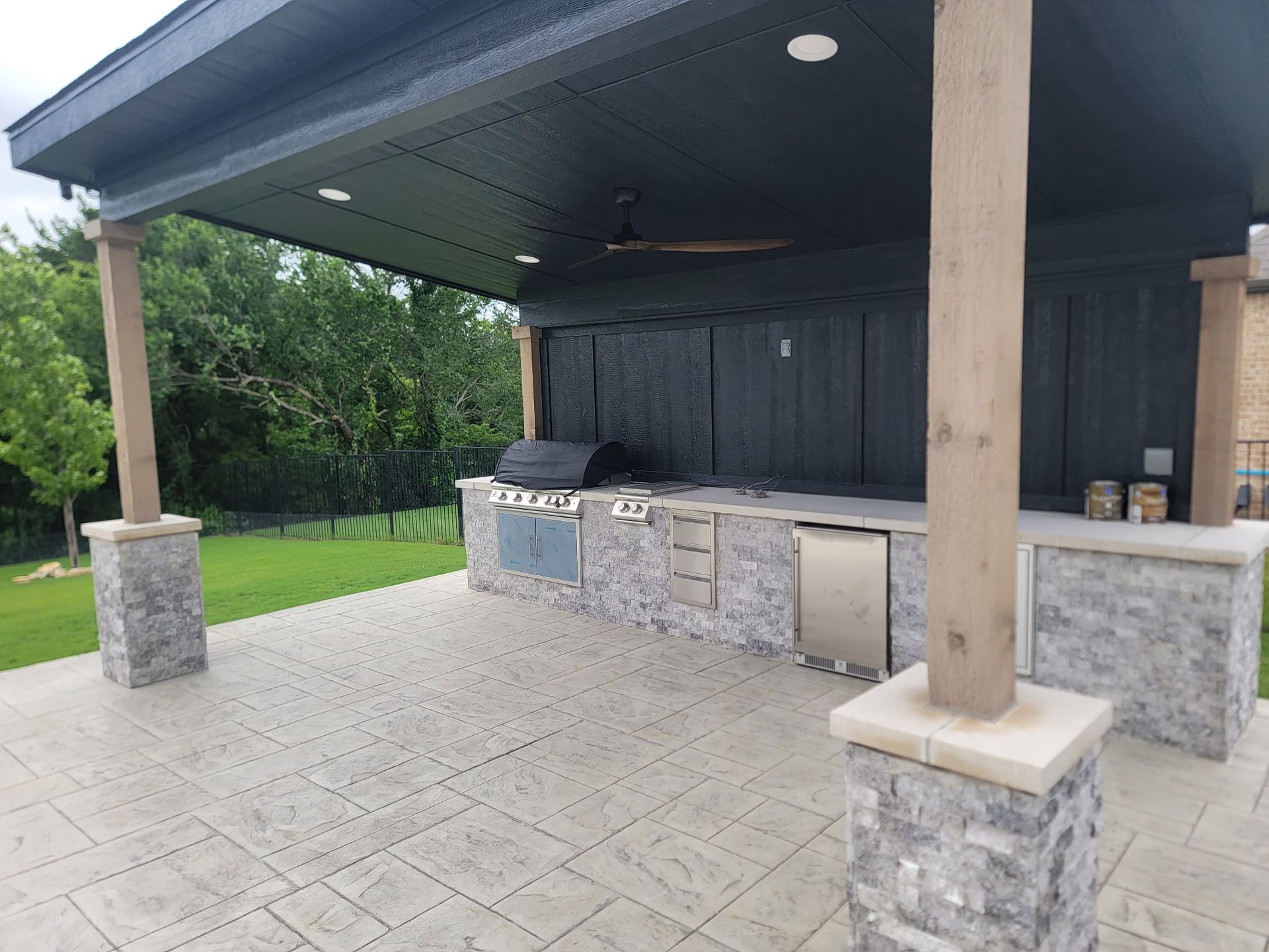 Outdoor covered patio with built-in grill and stone counters on a tiled floor