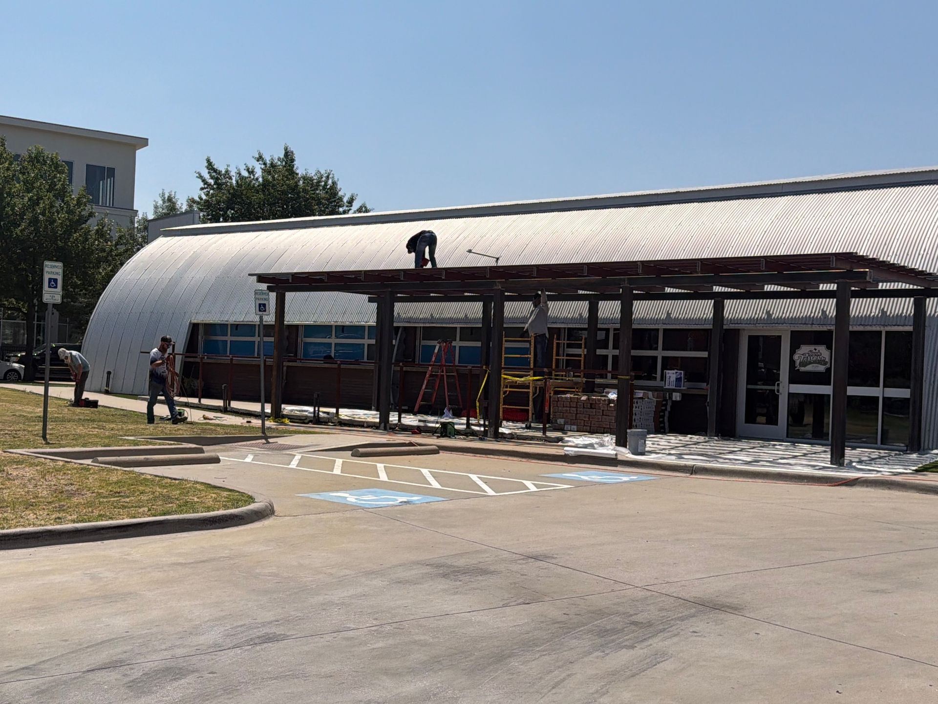 Click To See Roanoke Tavern's New Pergola Exterior of a low building with a covered entrance and parking lot, on a sunny day