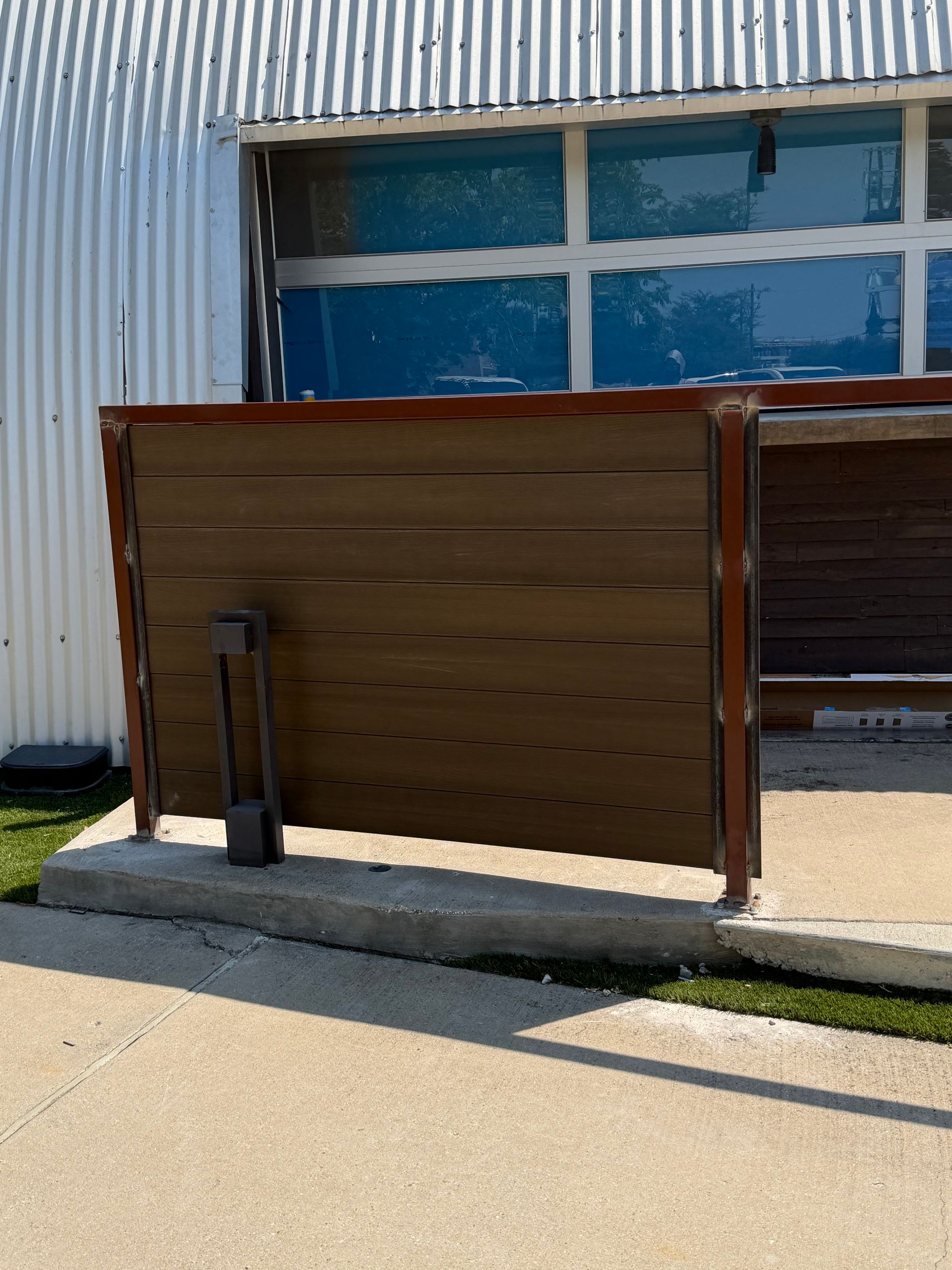 Wooden fence beside a corrugated metal building with a blue-paned window and concrete walkway