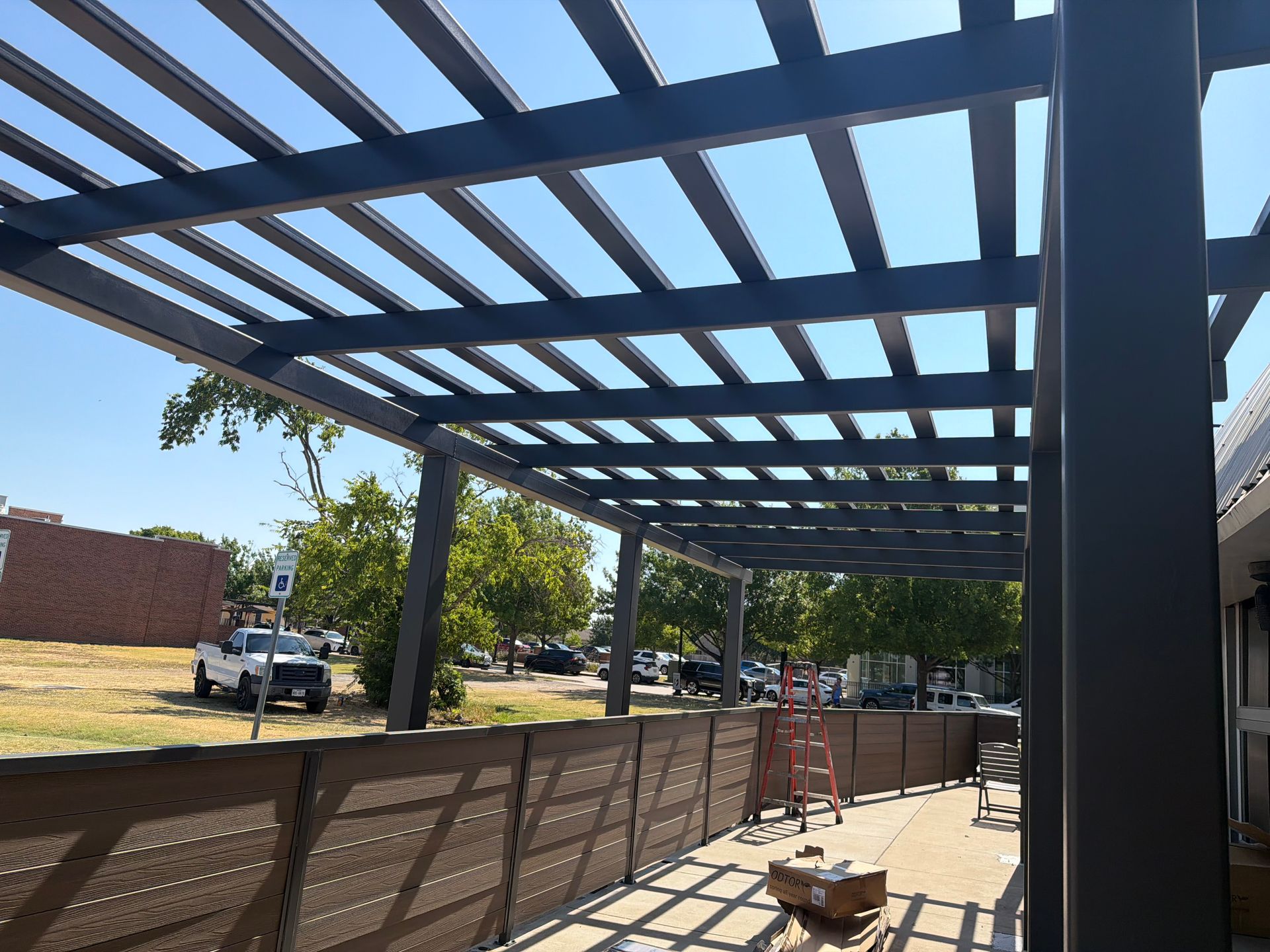 Covered outdoor walkway with a metal pergola, benches, and parked cars along the street