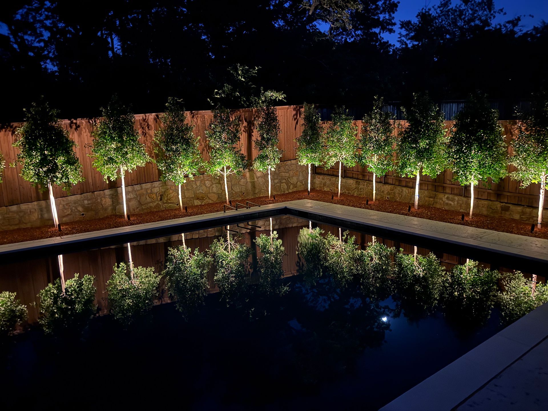 Nighttime reflecting pool with rows of illuminated small trees and brick walls around the water