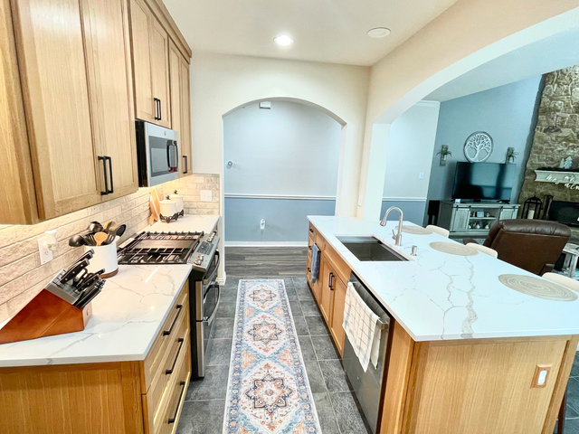 Bright kitchen with wood cabinets, white countertops, island, and an open view to a living room