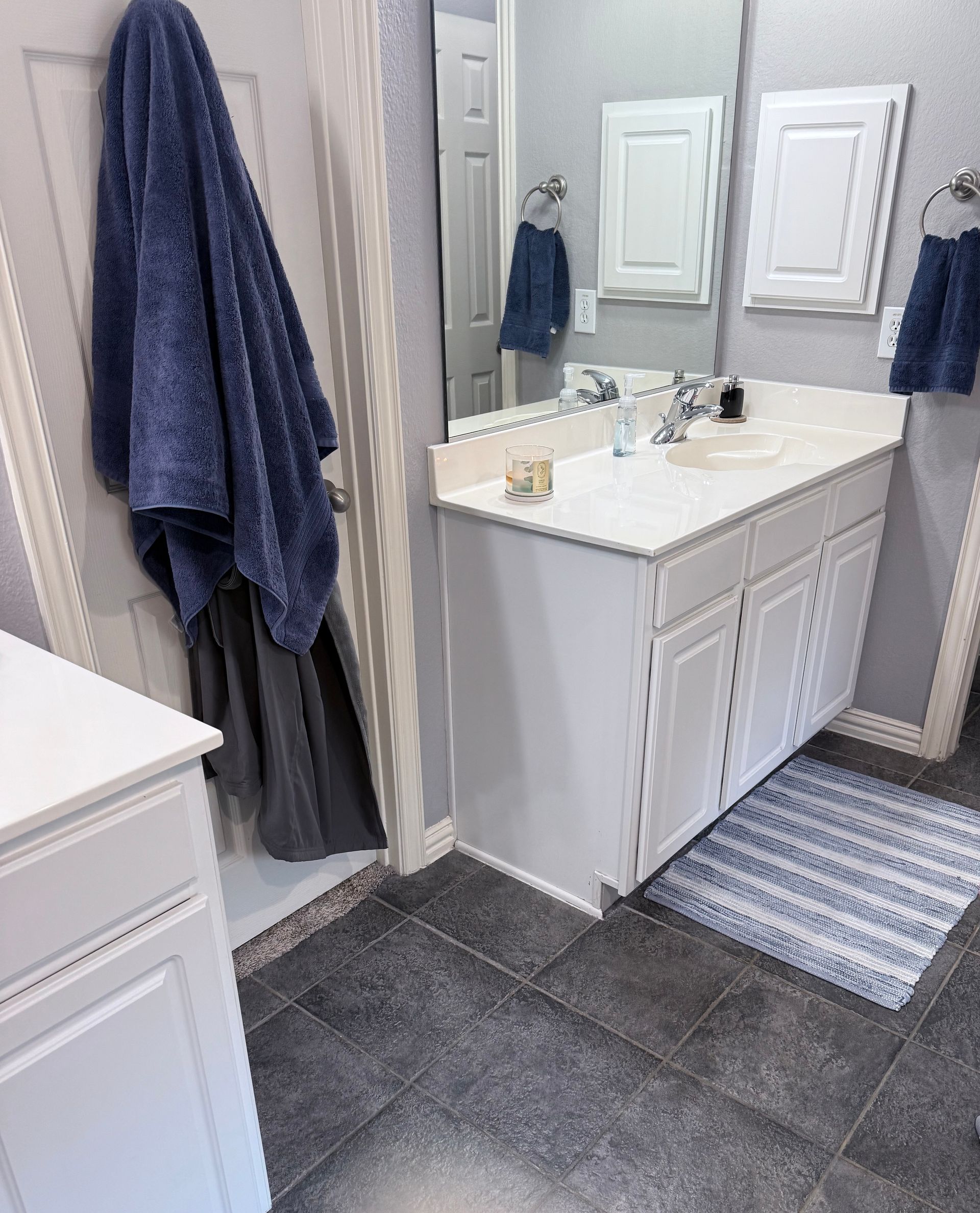 Bathroom vanity with mirror, dark gray tile floor, blue towels, and striped bath mat