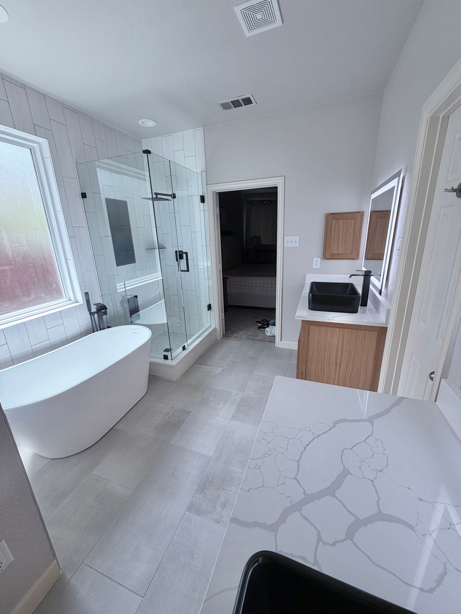 Bright modern bathroom with freestanding tub, glass shower, double vanity, and marble-patterned tile floor
