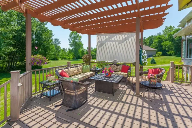 Outdoor patio with wicker seating, red cushions, and a wooden pergola in a sunny garden