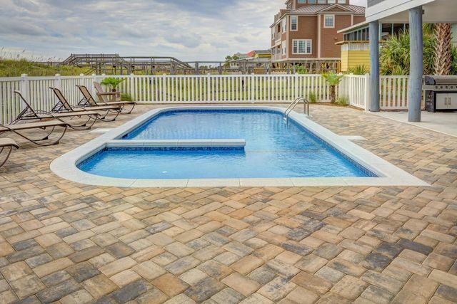 Backyard patio with a small blue swimming pool, lounge chairs, and white railing under cloudy skies