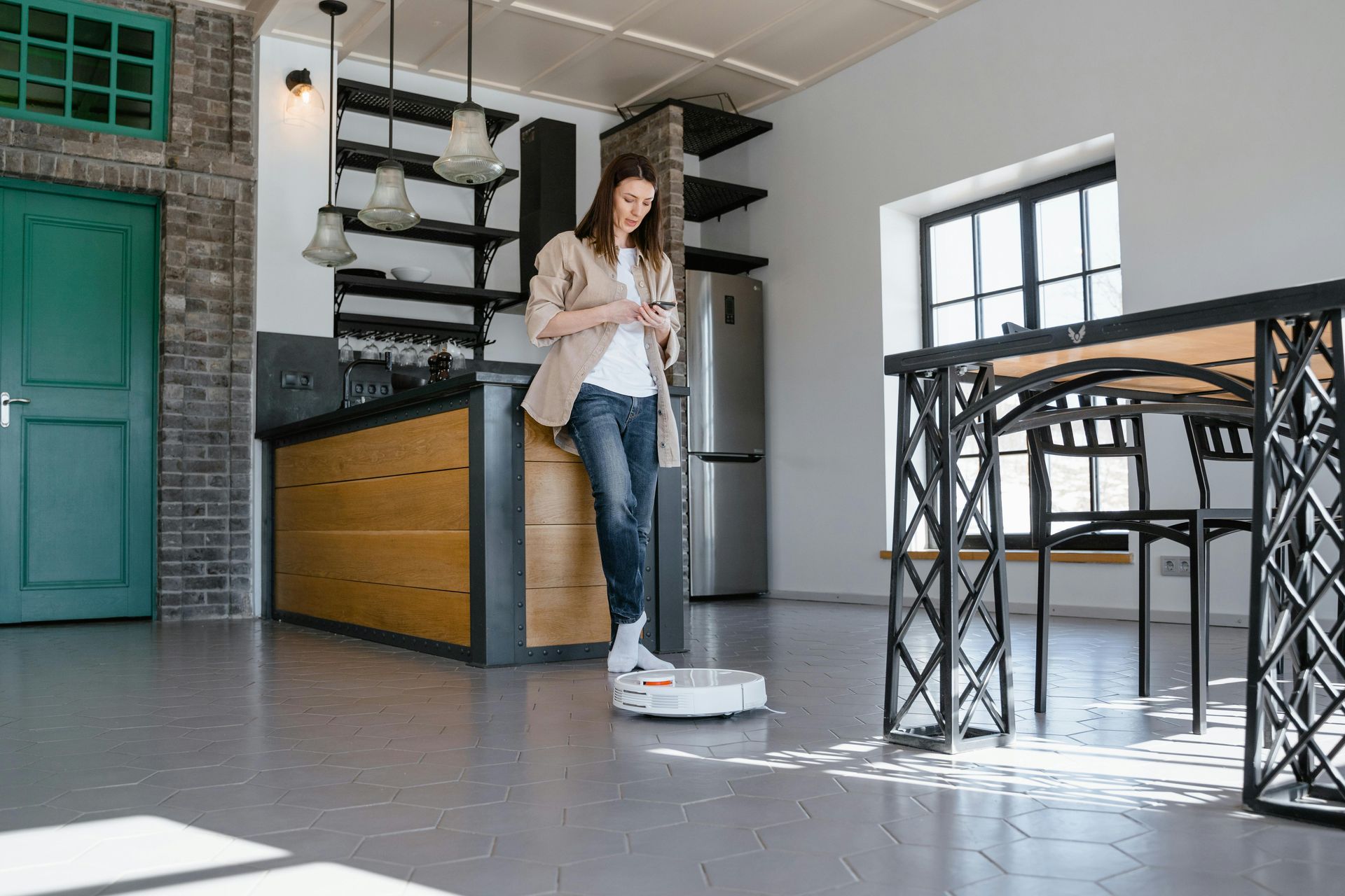 Woman mopping a bright kitchen floor beside a black island and teal door