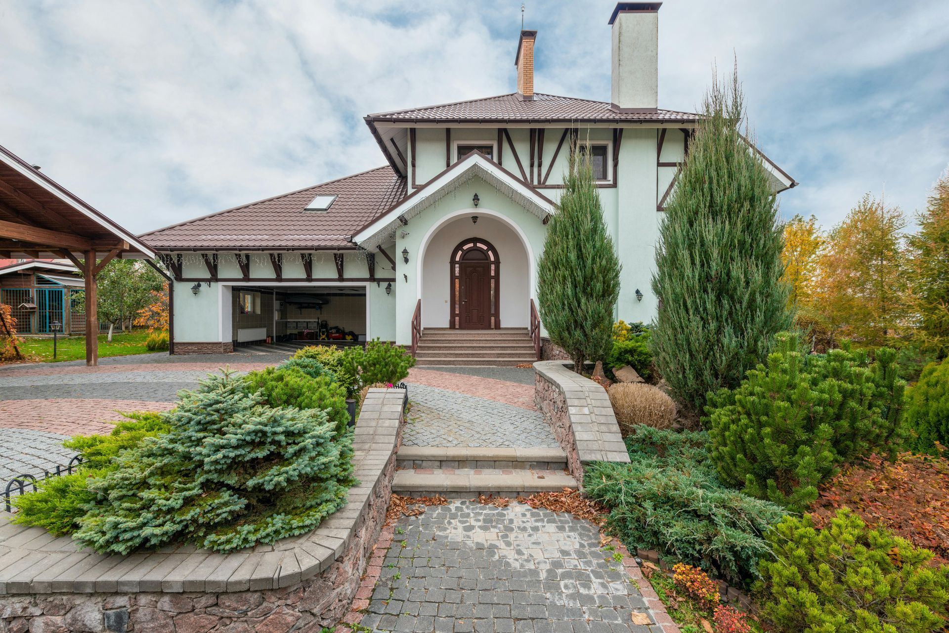 Elegant house with stone steps, arched entry, and landscaped front yard under a cloudy sky