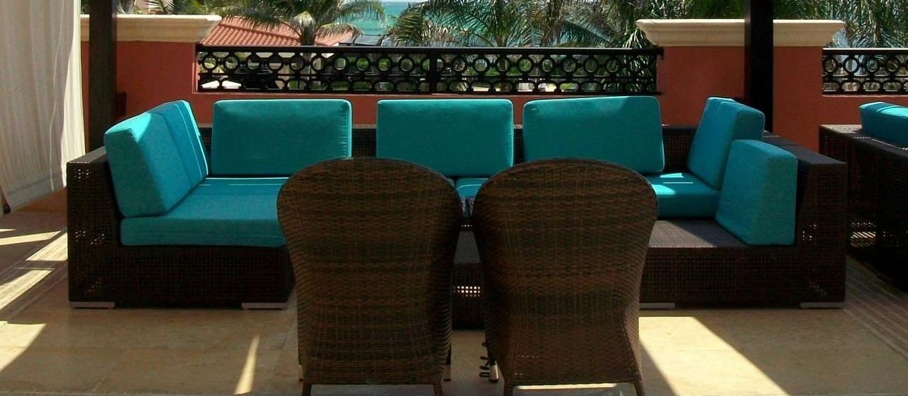A patio lounge area featuring a dark wicker sectional sofa with bright teal cushions and two matching wicker chairs.