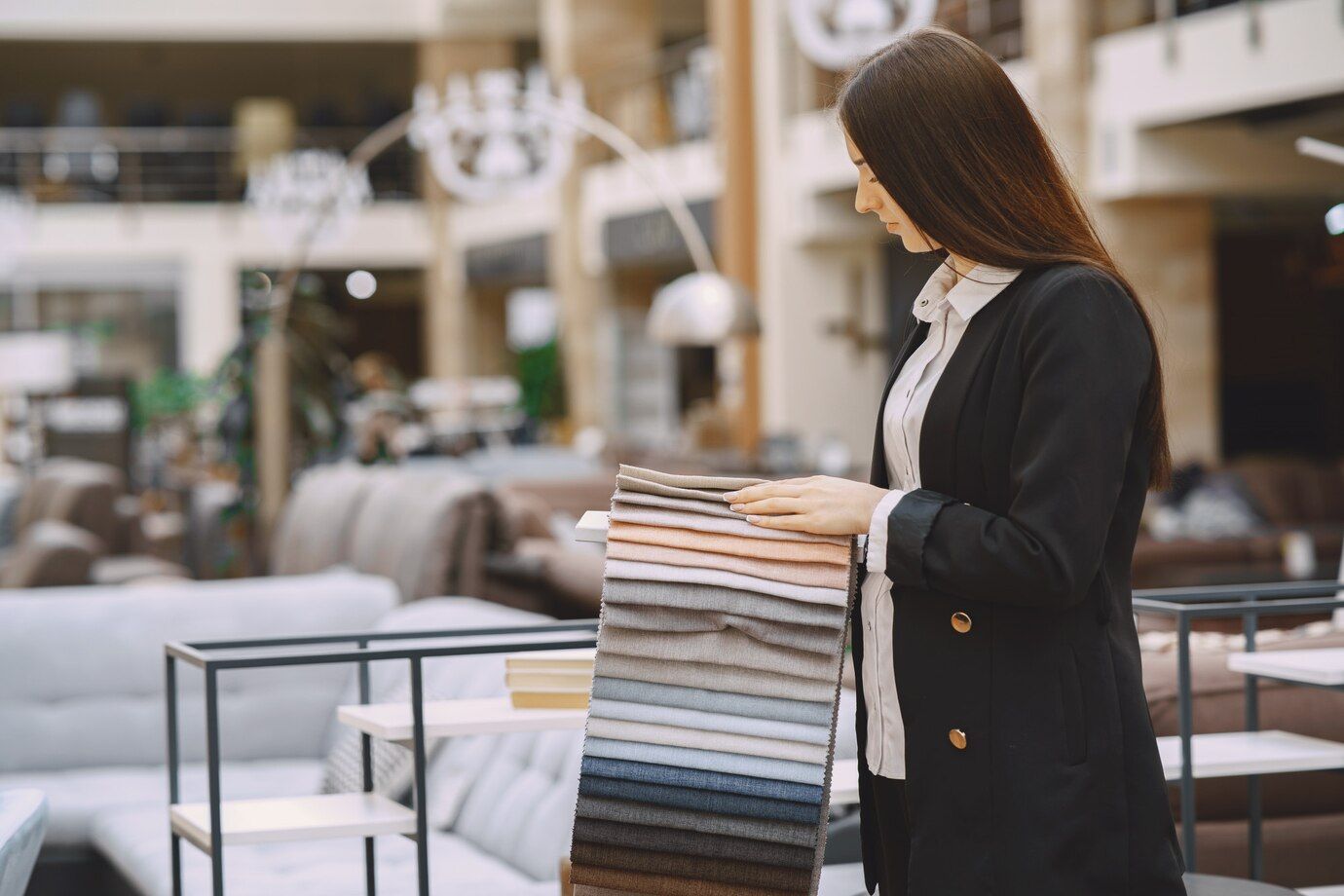 A person in a black blazer examines a stack of fabric swatches inside a furniture store.