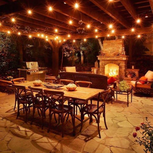 Cozy outdoor patio with long wooden table, string lights, and glowing fireplace at night