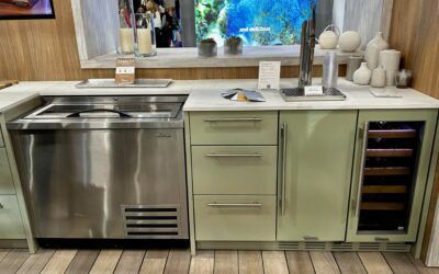Modern kitchen with stainless steel sink, pale green cabinets, and a built-in wine cooler under a window