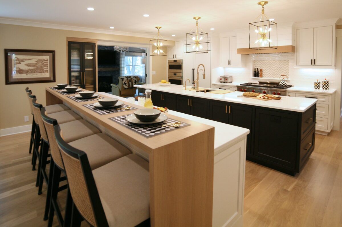 Elegant kitchen with a long island set for dining, white cabinets, dark island, and hanging pendant lights