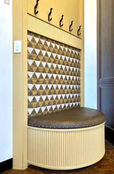 Corner mudroom bench with hooks, patterned tile backsplash, and rounded cushioned seat
