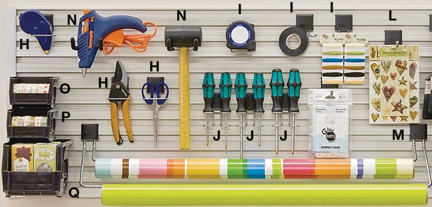Wall-mounted organizer with labeled art supplies, tools, tape, scissors, and rolls of colored paper