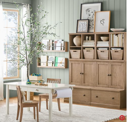 Bright, minimalist playroom with wooden table, chairs, shelves, storage baskets, and a leafy plant by the window