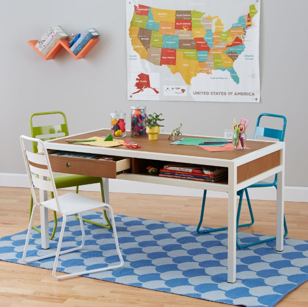Children’s play table and chairs on a blue rug, with a U.S. map on the wall and toy books on the shelf