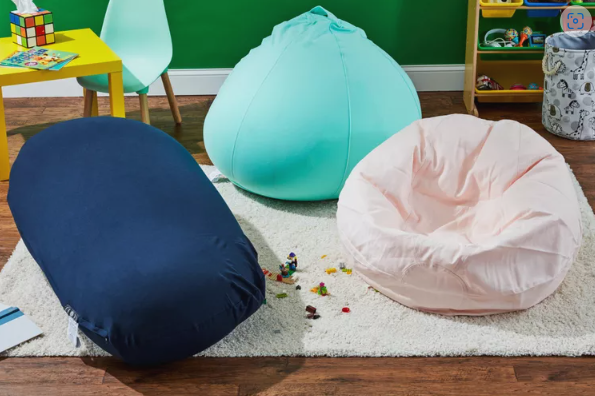 Three colorful bean bags on a rug beside a small table and chair.