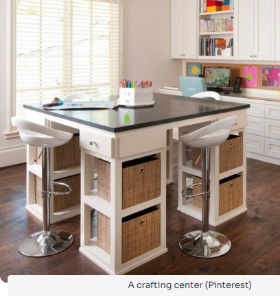Bright craft center with black worktable, white cabinets, stools, and woven storage baskets by a window