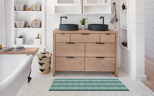 Modern bathroom with a wooden vanity, twin black sinks, and a green striped rug.