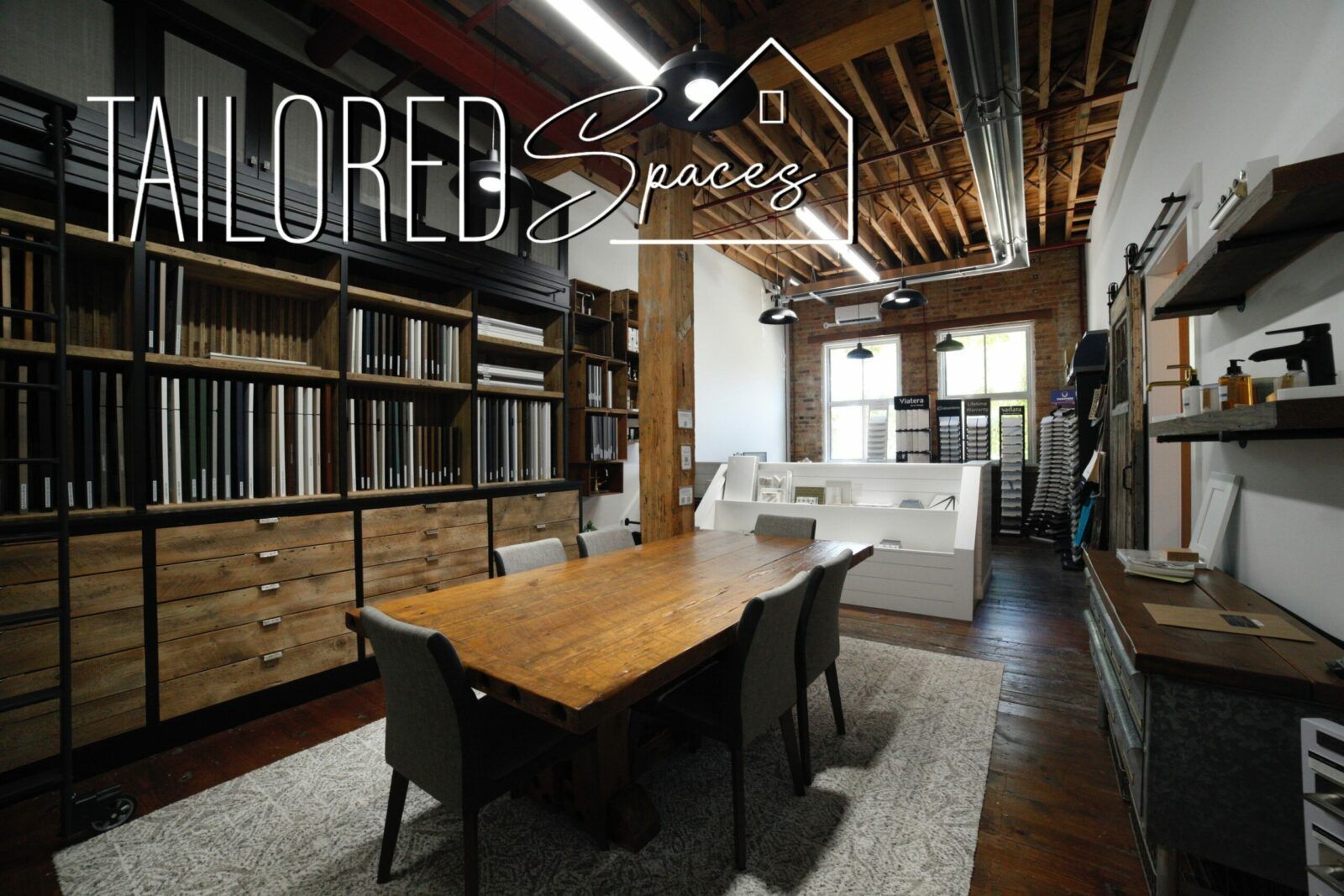 Loft office with long wooden table, black chairs, shelves, and exposed beams, labeled “Tailored Spaces”