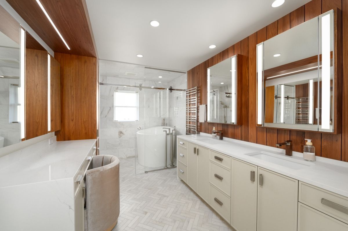 Bright white bathroom with large mirrors, double sinks, wood accents, and a towel basket