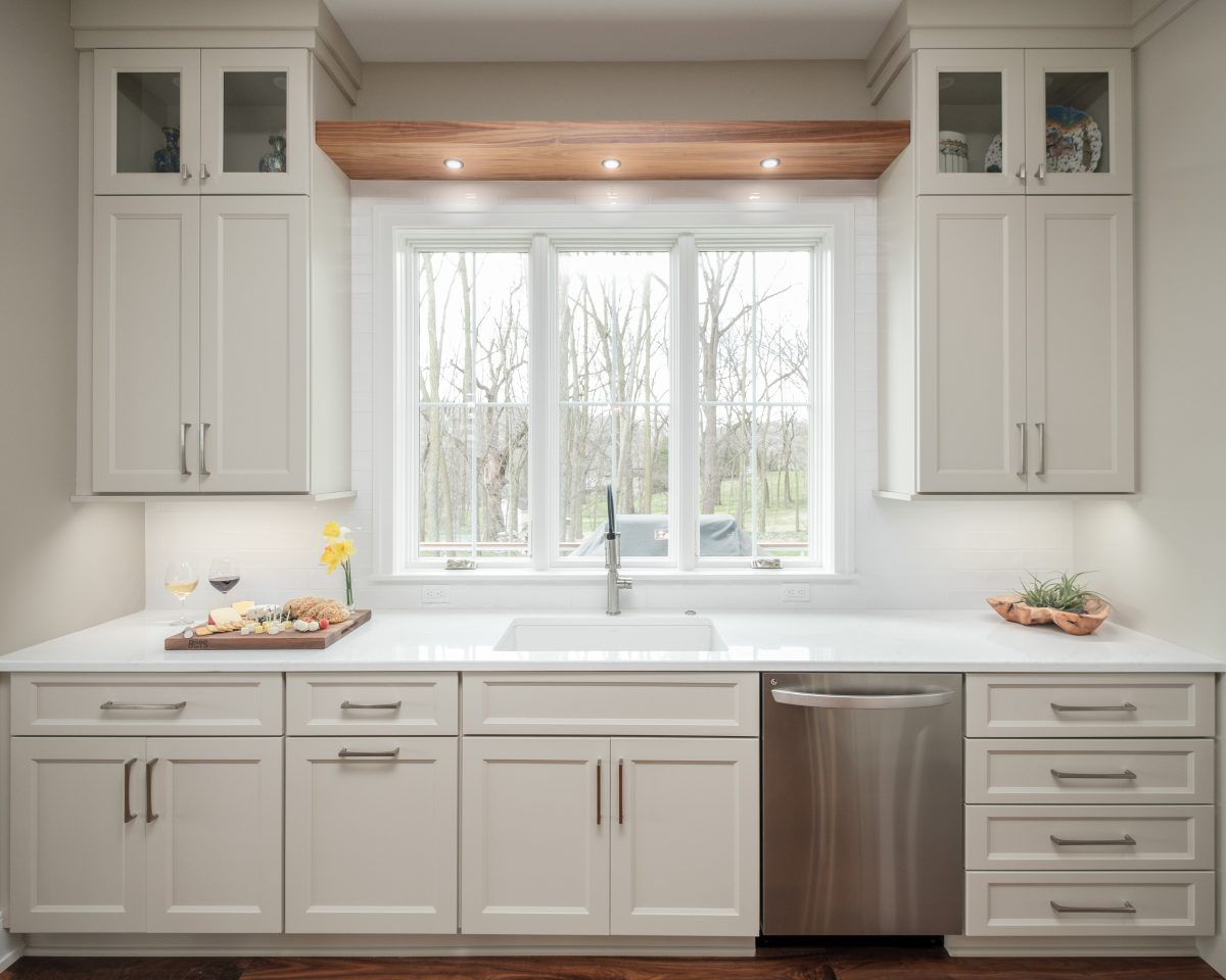Bright white kitchen with cabinets, marble counters, stainless dishwasher, and a window above the sink