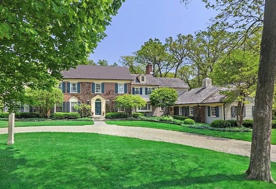 Large brick house with a curved driveway, green lawn, and trees in front.